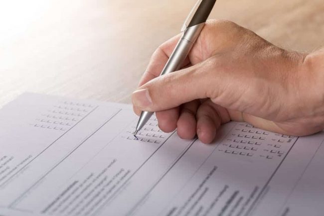 close-up of a man holding a pen filling out a paper survey