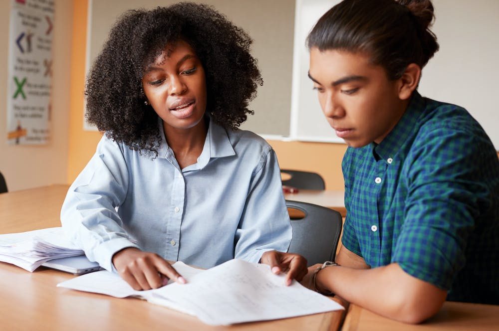 Tutor helping student by showing them something within a book